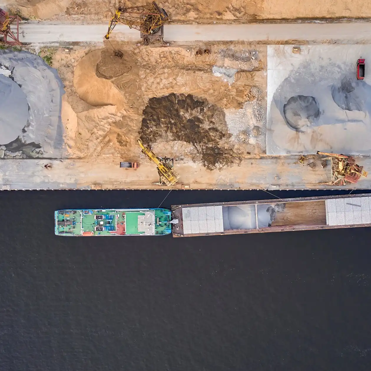 Aerial view of a cargo ship at a pier beside heaps of construction aggregate
