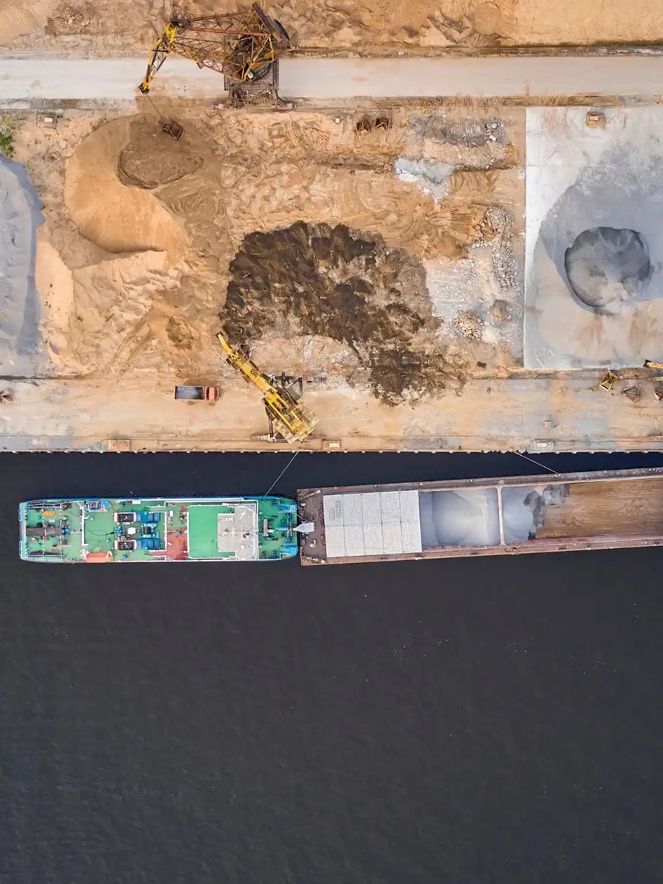Aerial view of a cargo ship at a pier beside heaps of construction aggregate