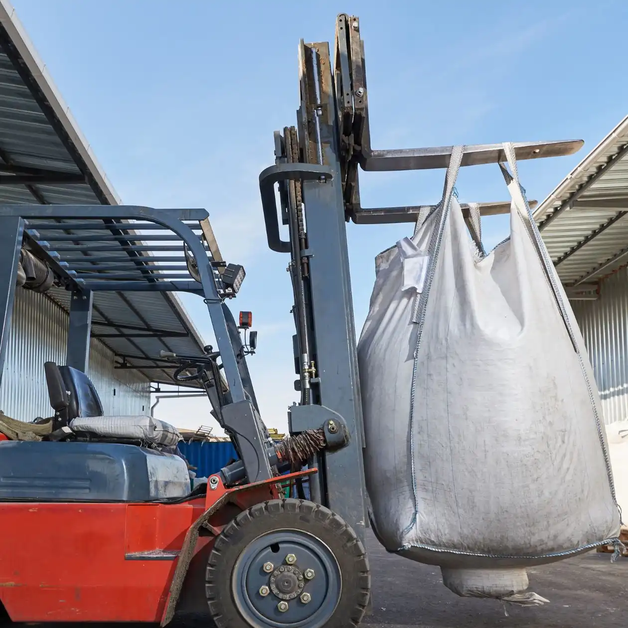 A forklift lifting a large white bulk bag of fertilizer in a port yard