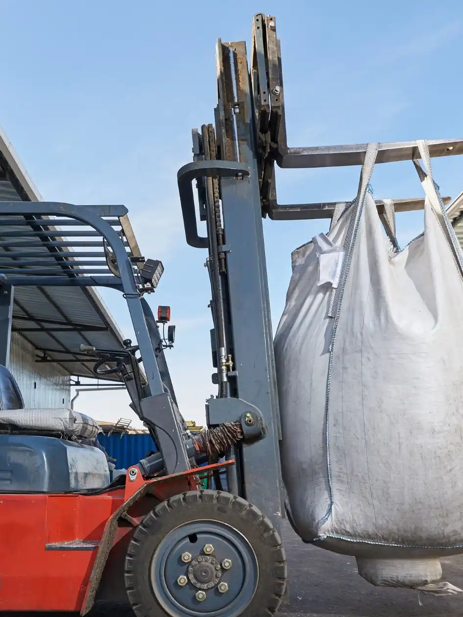 A forklift lifting a large white bulk bag of fertilizer in a port yard