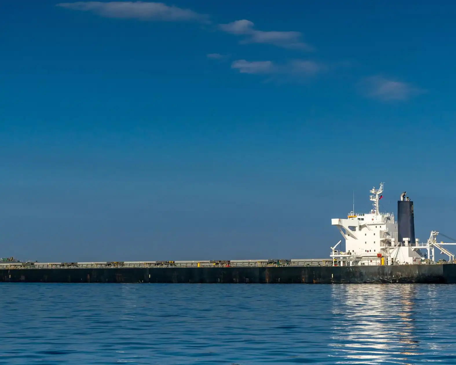 A black-and-white bulk carrier underway on calm blue water under a clear sky