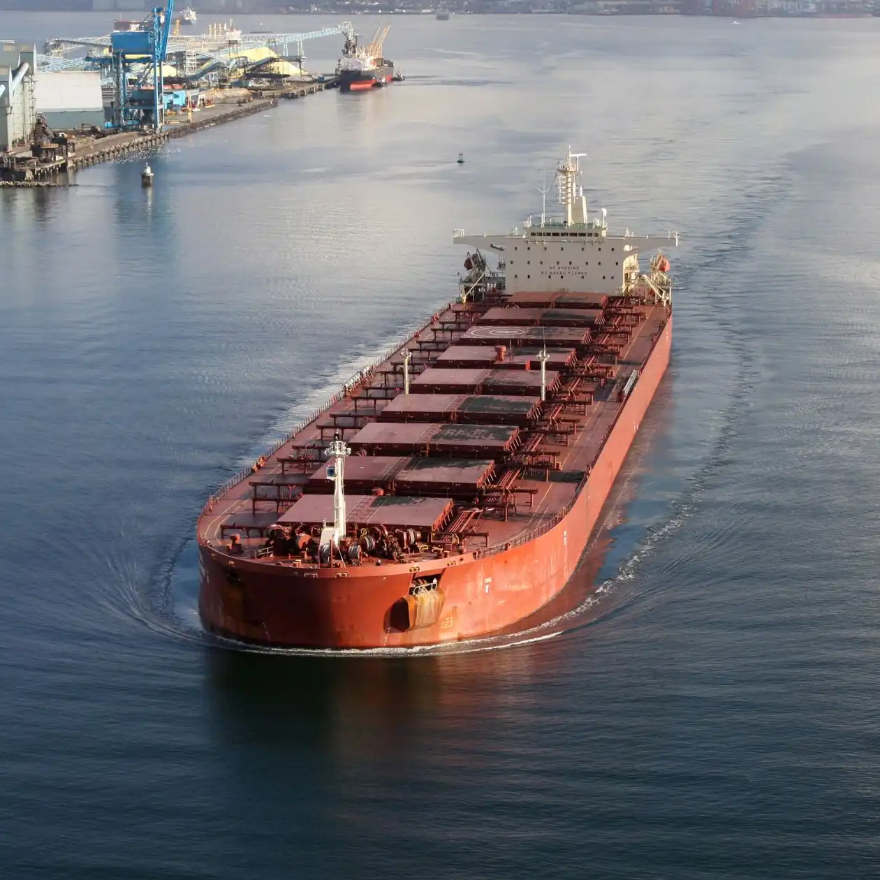 Aerial view of a red Panamax-size bulk carrier approaching a port