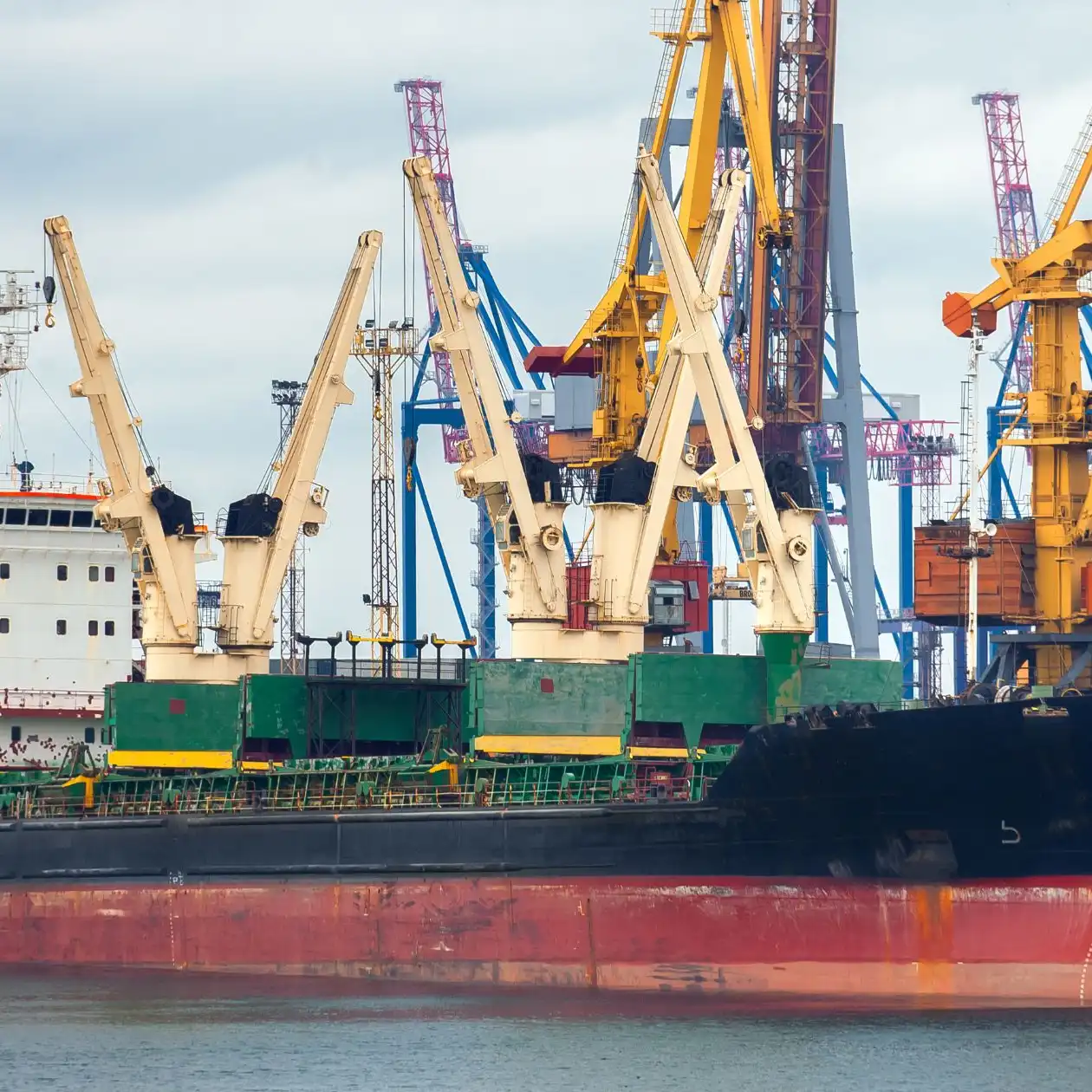 A bulk carrier docked at a busy industrial port with loading cranes