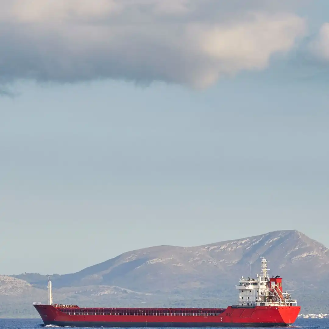 A bulk carrier underway in ballast on calm water with a coastline behind