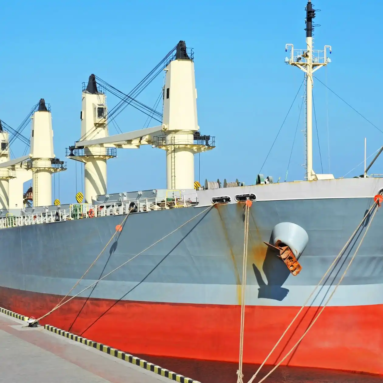 A geared bulk carrier with open hatches and deck cranes in port