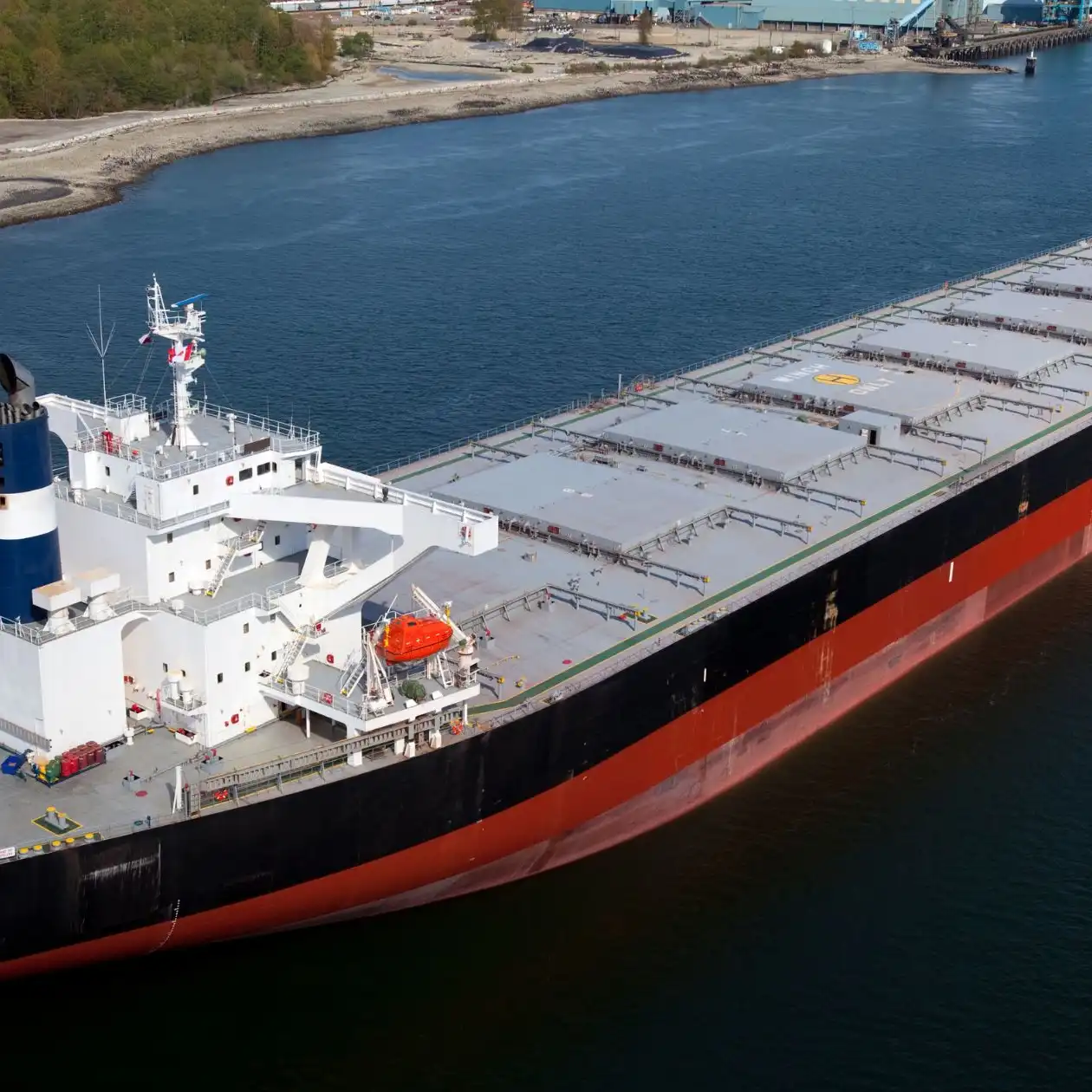 A small bulk carrier with flat hatch covers underway near a coastline