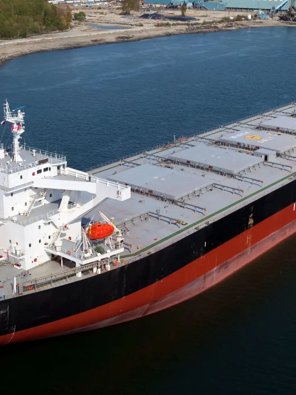 A small bulk carrier with flat hatch covers underway near a coastline