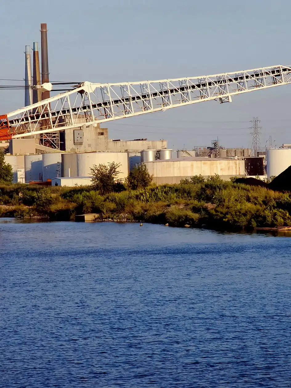 A red bulk carrier at an industrial berth beside a dark bulk pile and conveyor