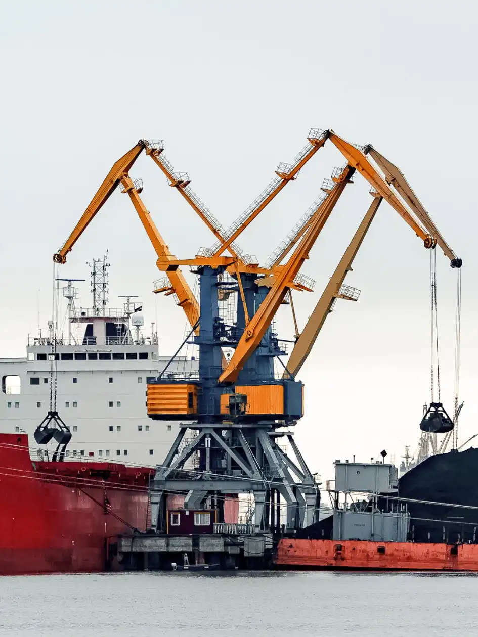 A red bulk carrier with yellow cranes handling thermal coal at a port