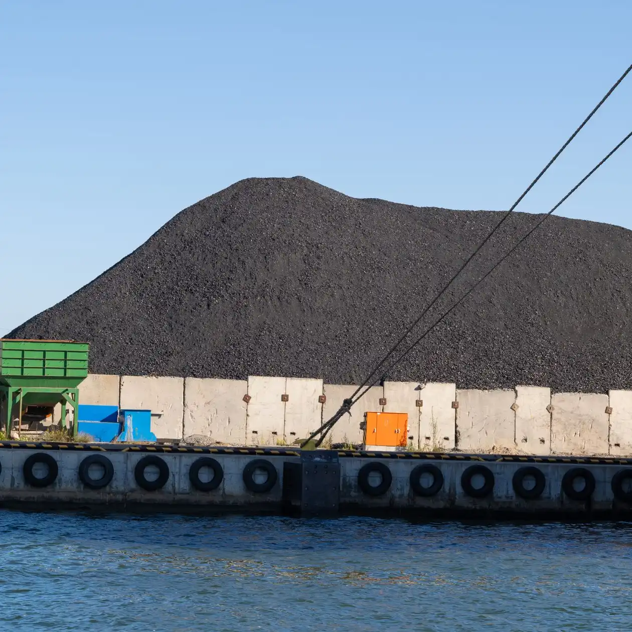 A large coal stockpile at a port with a moored bulk carrier alongside