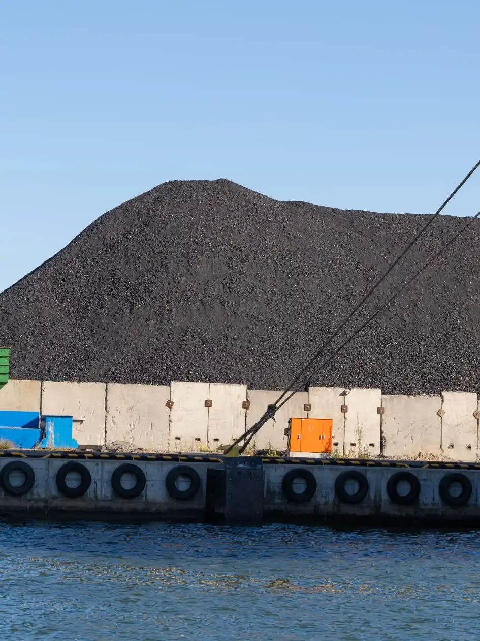A large coal stockpile at a port with a moored bulk carrier alongside