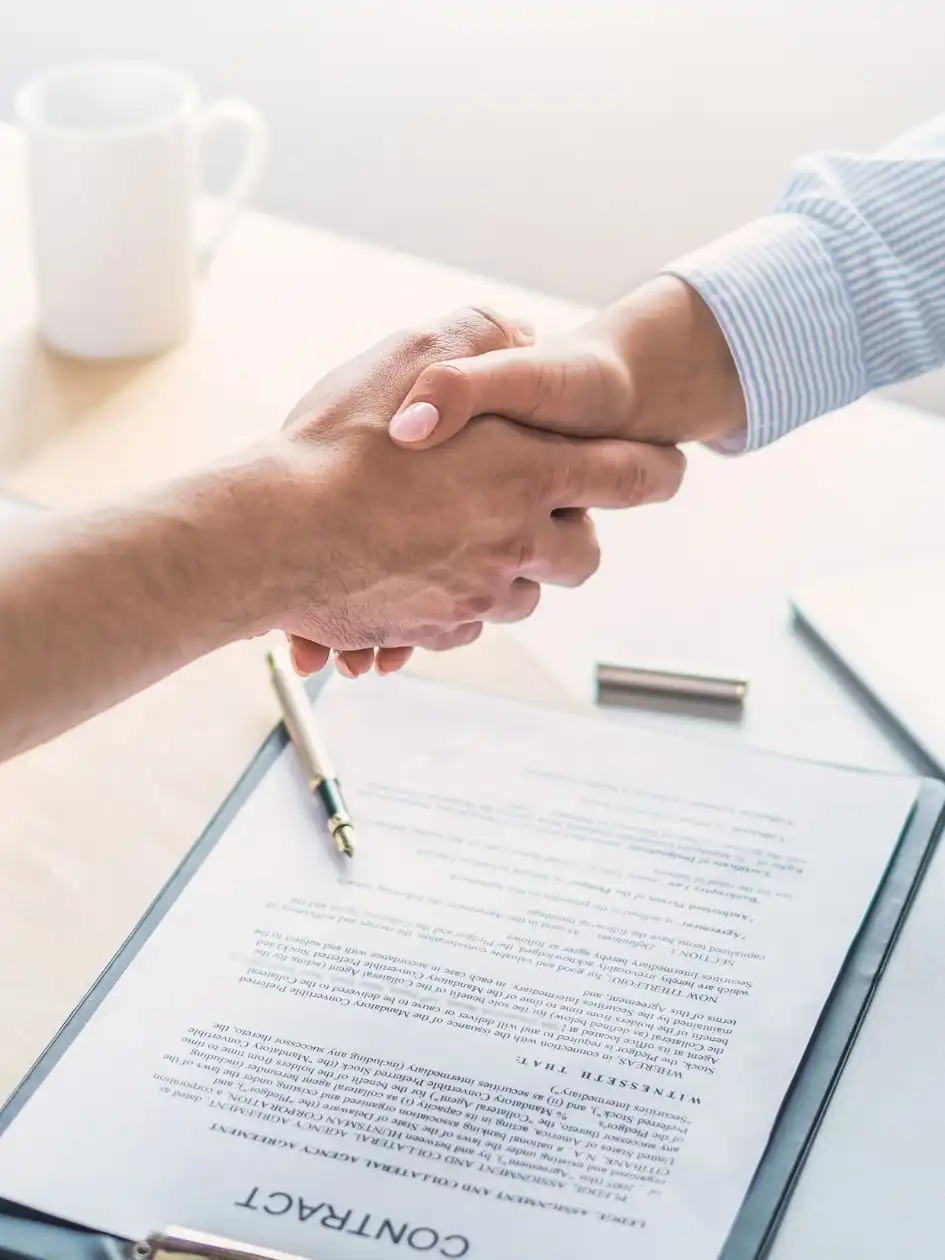 Two people at a ship chartering company shaking hands over a desk with charter party documents and a pen