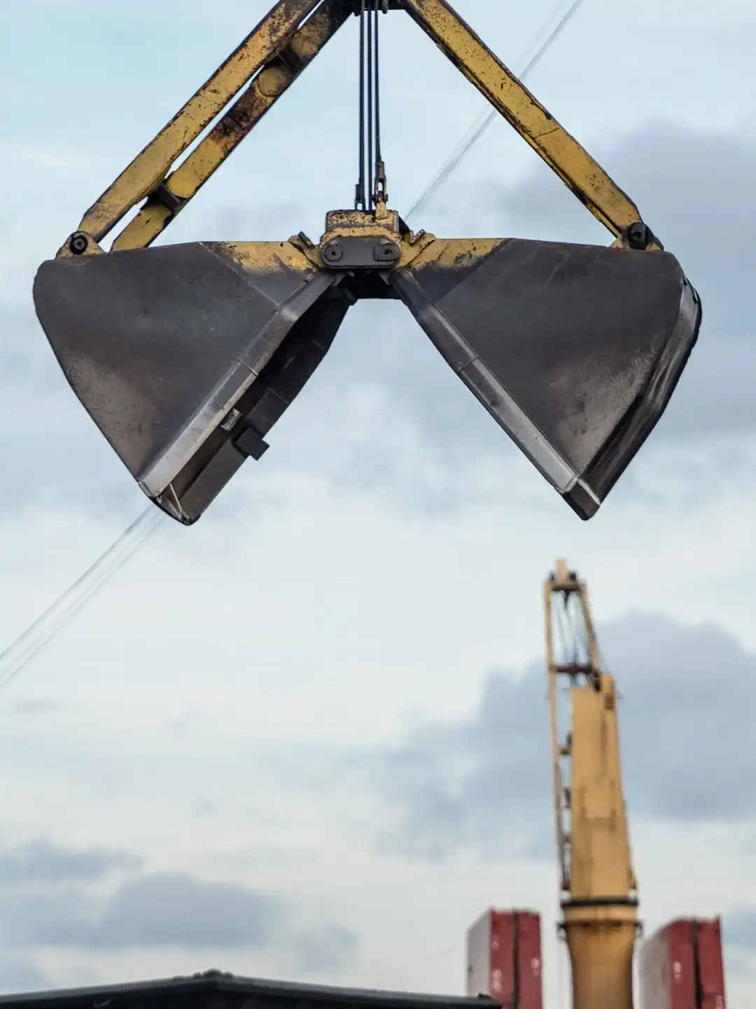 An open clamshell grab claw hanging from a crane at a port berth