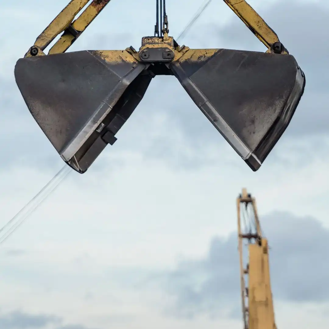 An open clamshell grab claw hanging from a crane at a port berth