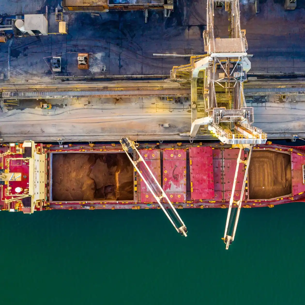Aerial view of a bulk carrier with open holds and shore cranes loading grain