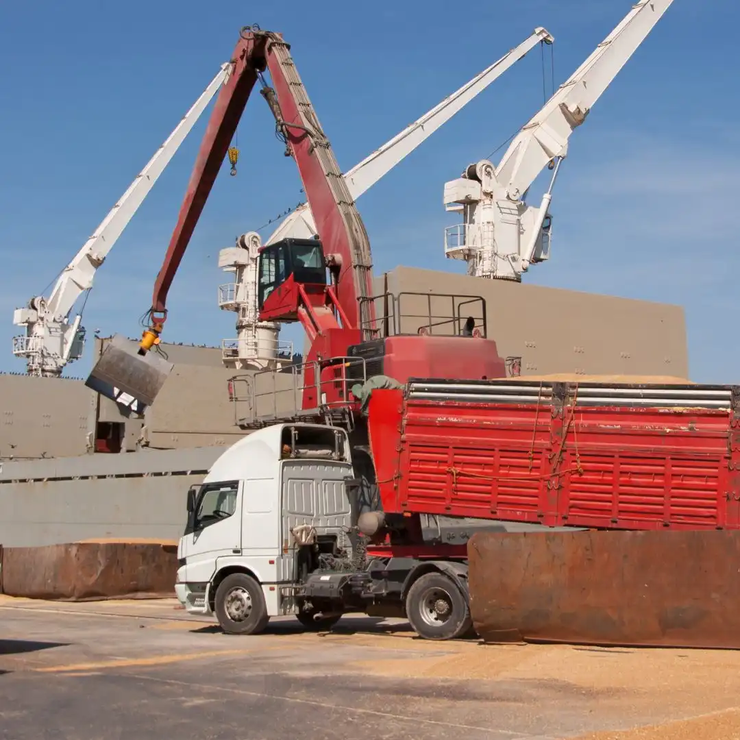 A crane loading grain onto a cargo ship beside a truck at a terminal