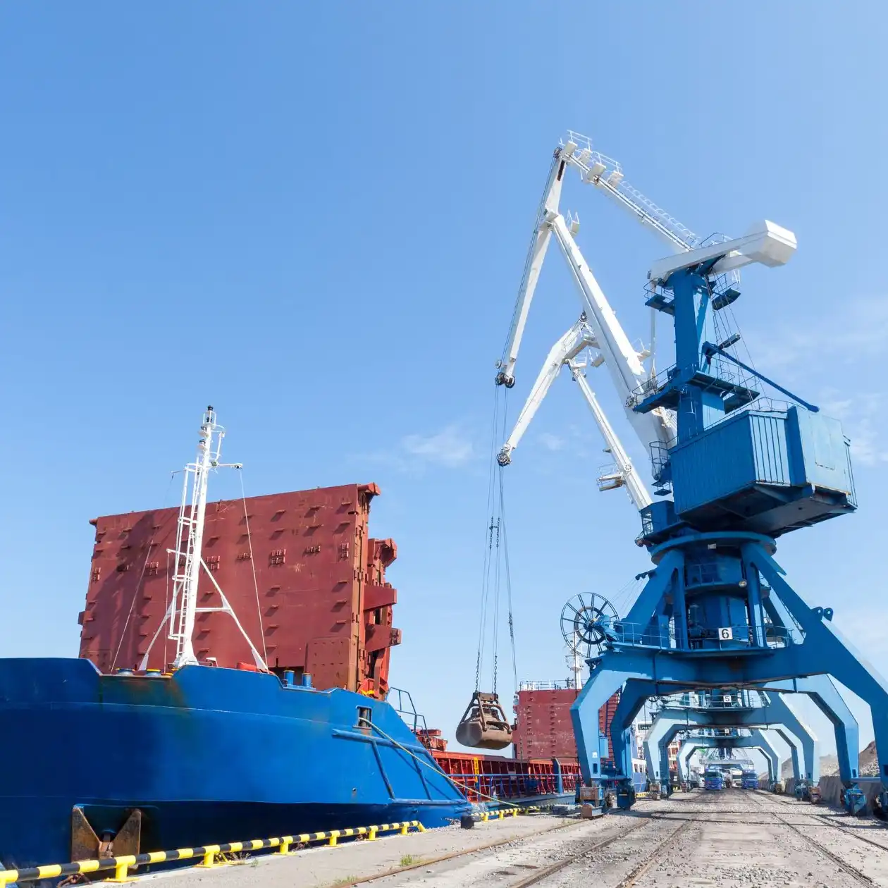 A bulk carrier with deck cranes loading granular bulk material at a port