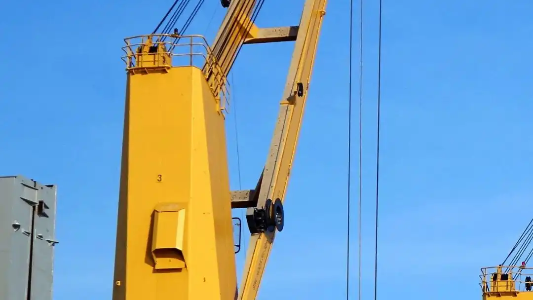 A yellow heavy-lift deck crane on a project-cargo vessel against a clear sky