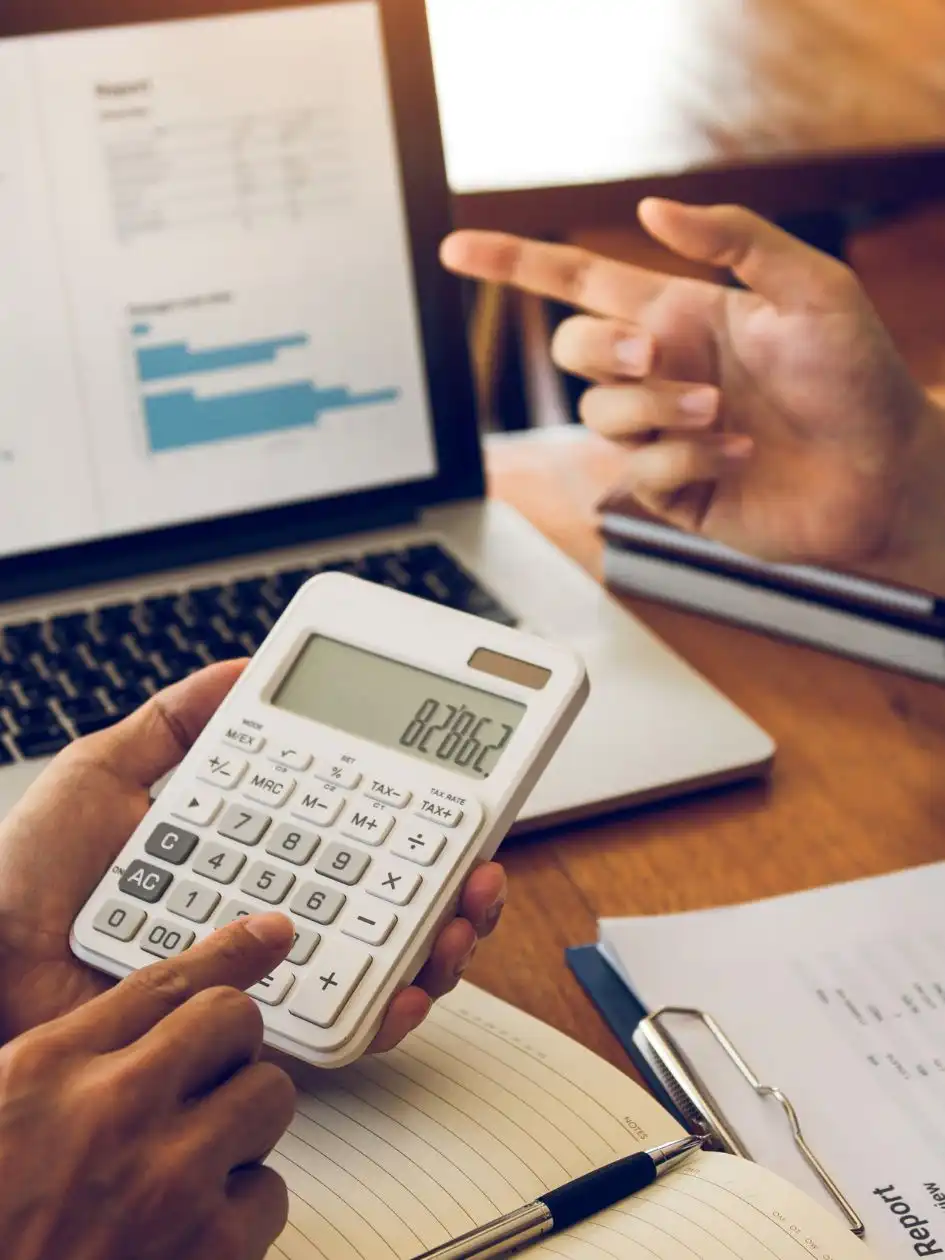 Two brokers reviewing freight figures on a laptop with a calculator, charts and a report on the desk