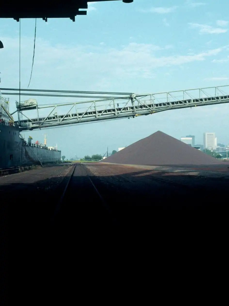 A ship at a harbour with a shoreside conveyor loading bulk ore onto a pile