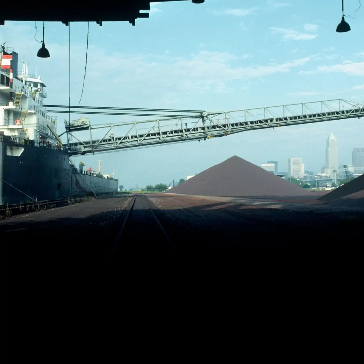 A ship at a harbour with a shoreside conveyor loading bulk ore onto a pile