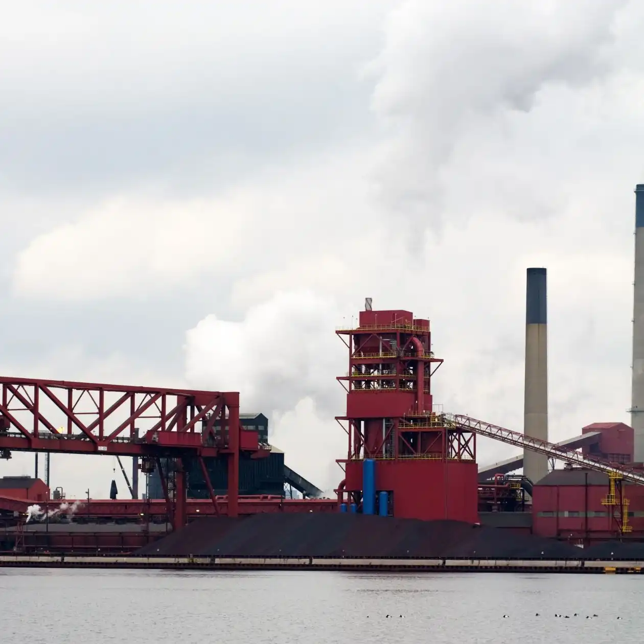 An ore export terminal with red conveyor structures beside the water