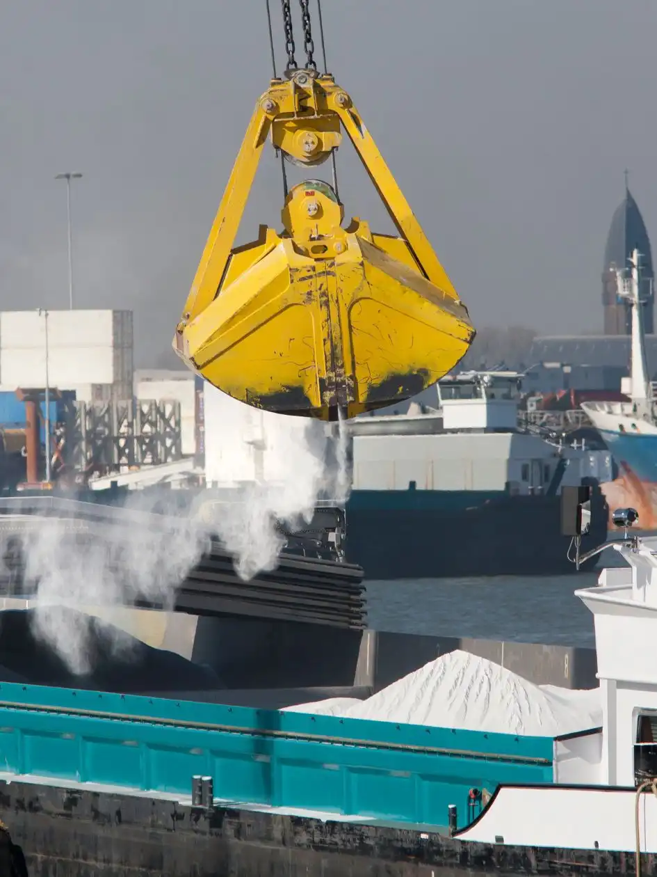 A ship at a port being loaded with powdered bulk material by a yellow crane