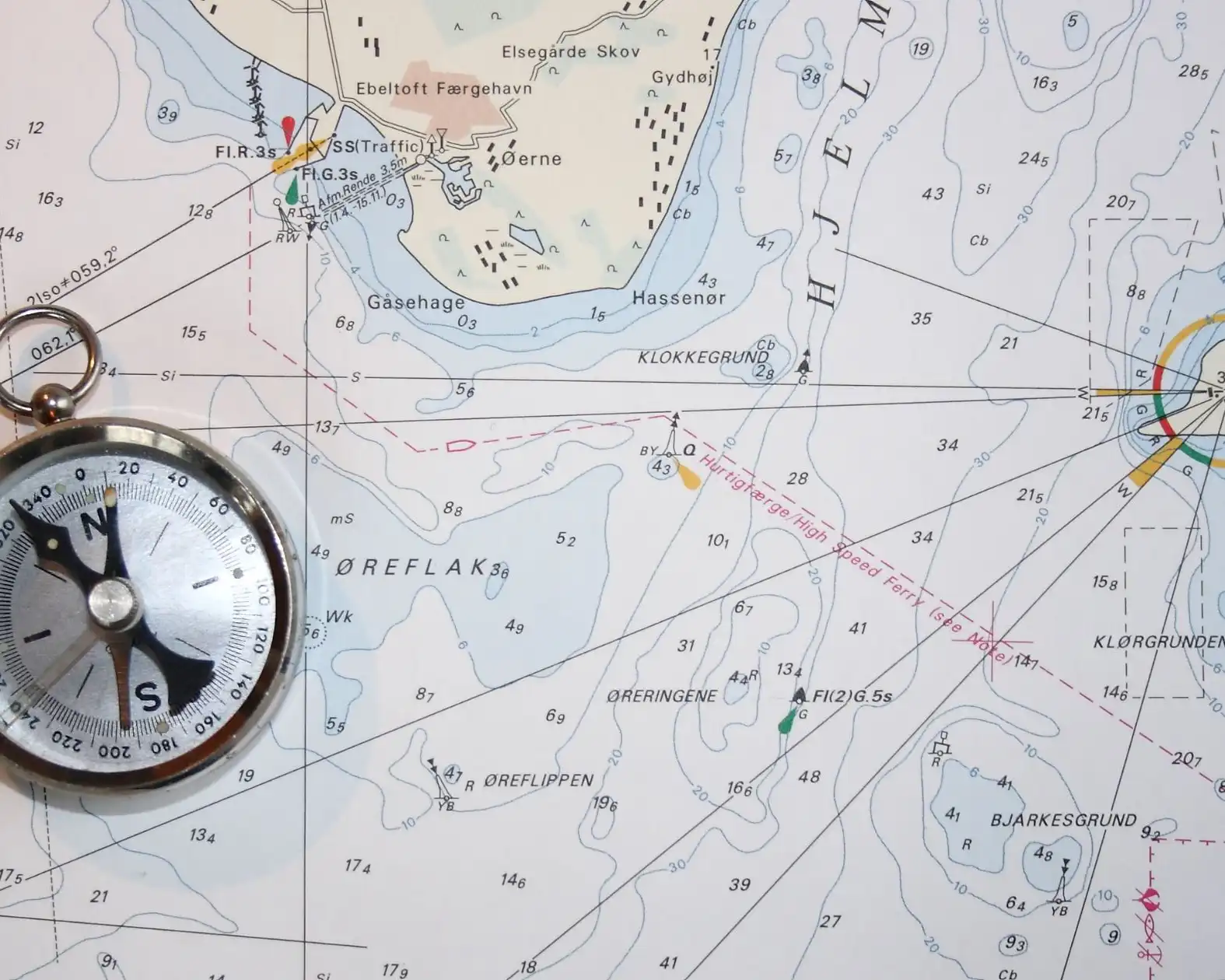 A compass resting on a detailed nautical chart marked with depths and routes