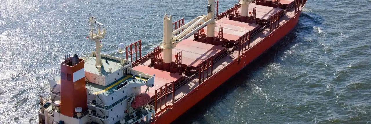 Aerial view of a red self-discharging bulk carrier with deck cranes underway