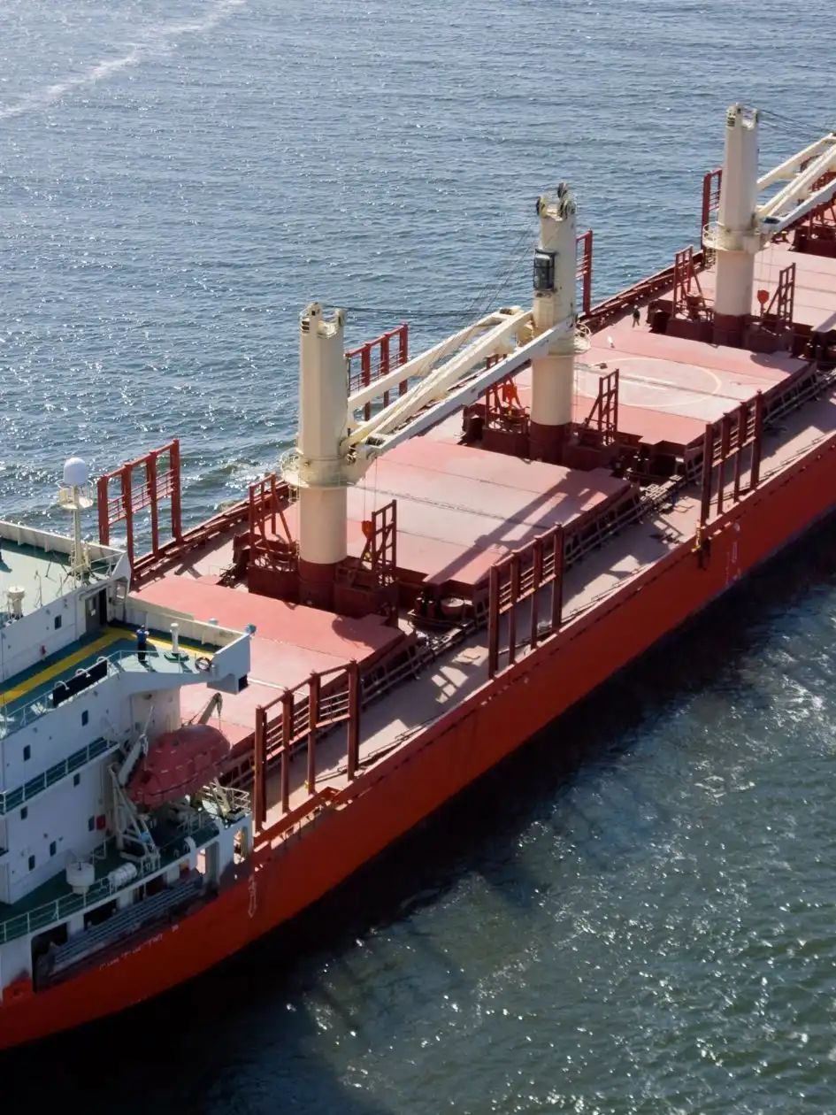 Aerial view of a red geared bulk carrier with deck cranes underway