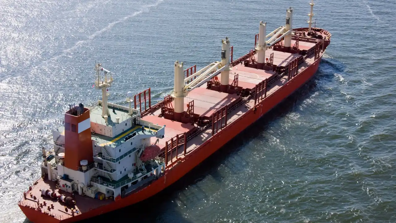 Aerial view of a red self-discharging bulk carrier with deck cranes underway