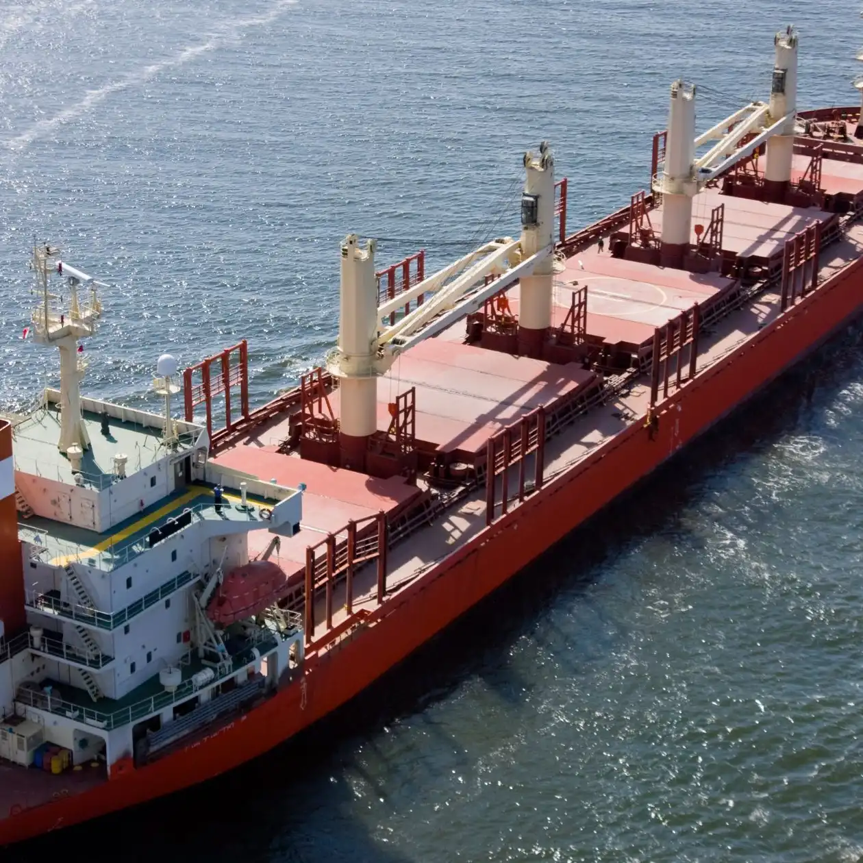 Aerial view of a red geared bulk carrier with deck cranes underway