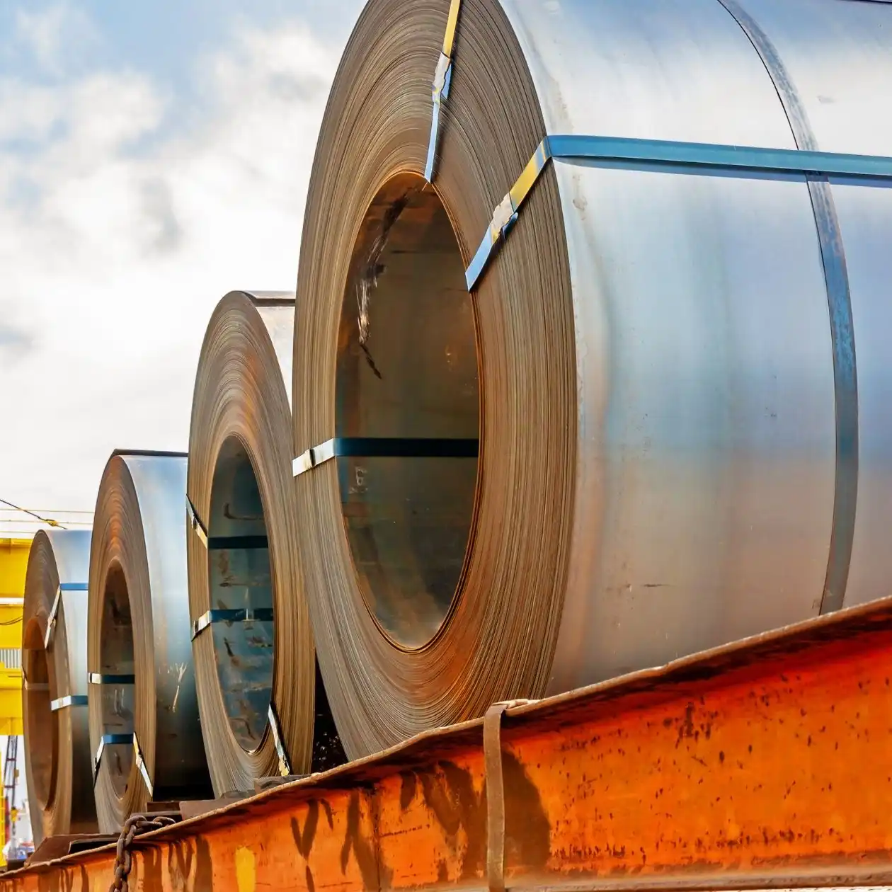 Rolls of steel coils lined up on a quay under a clear sky